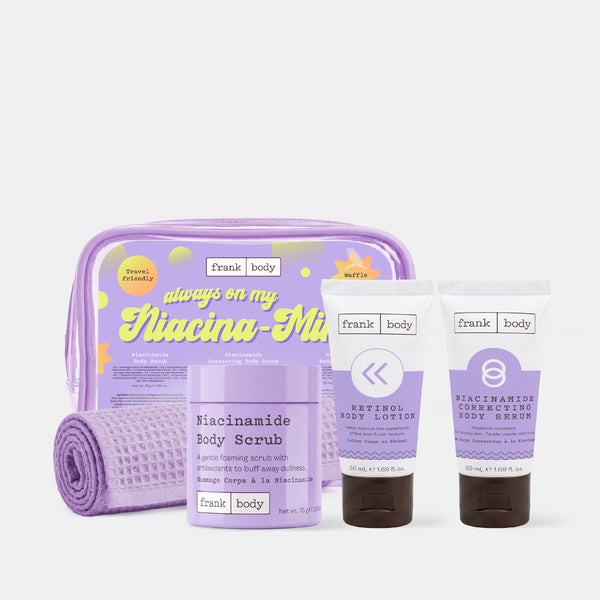 The frank body Always On My Niacina-mind Kit with the niacinamide body scrub, retinol body lotion and correcting body serum beside a lilac bag and towel on white.