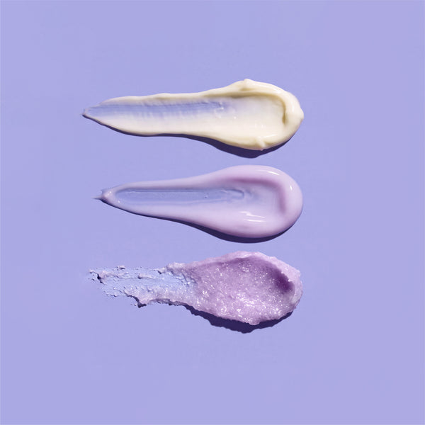 Three swatches from the frank body Always On My Niacina-mind Kit on a purple background: a cream lotion, a lilac serum and a glittery body scrub.