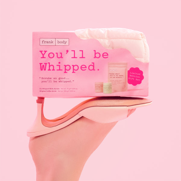 A hand holds a pink box labeled 'frank body You'll be Whipped.' against a solid pink background.