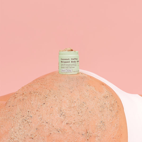 A small jar of whipped body butter sits on top of a textured peach-colored body with a light pink background.