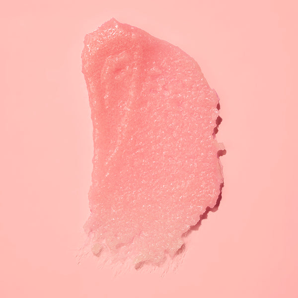 A textured smear of translucent pink cosmetic gel or scrub on a solid pink background.