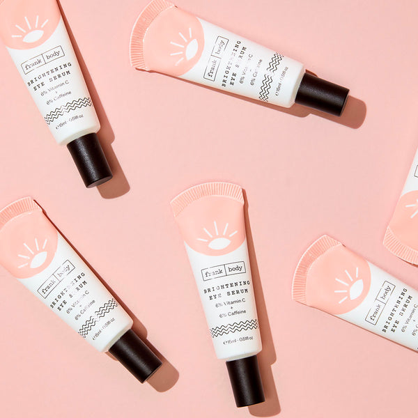 Tubes of frank body Brightening Eye Serum scattered on a pink background.