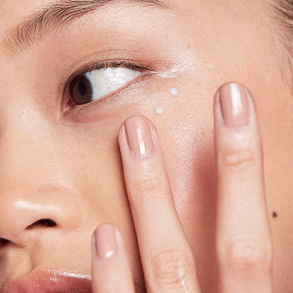 A woman patting frank body Brightening Eye Serum under her eye with a fingertip.